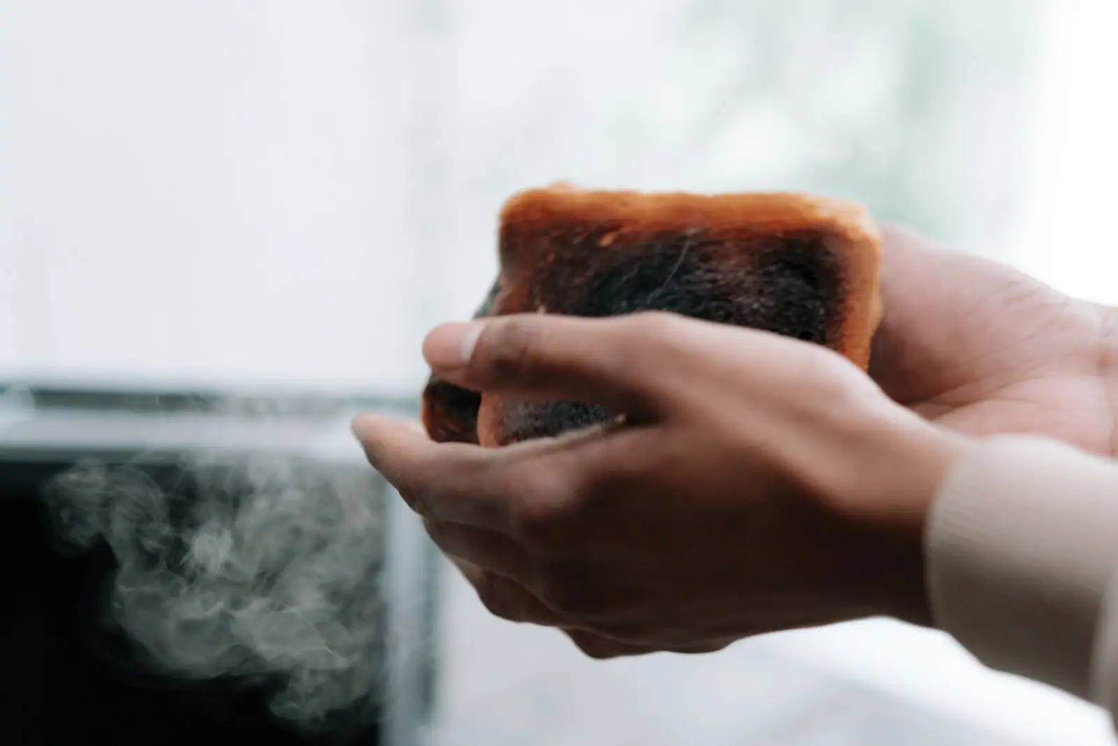 Hands holding a slice of burnt toast with smoke rising from it