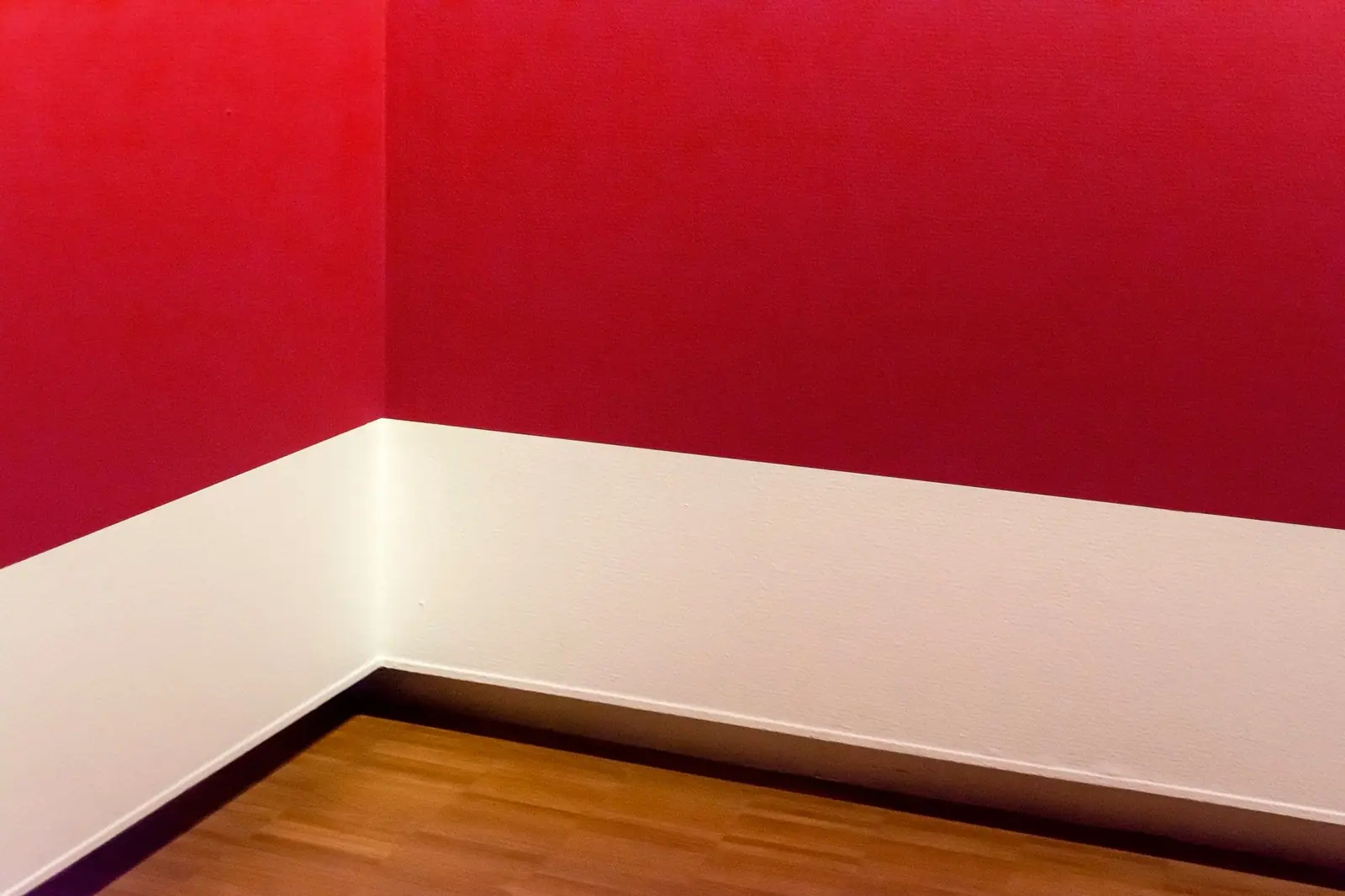 The corner where a white baseboard meets a red wall and a wooden floor