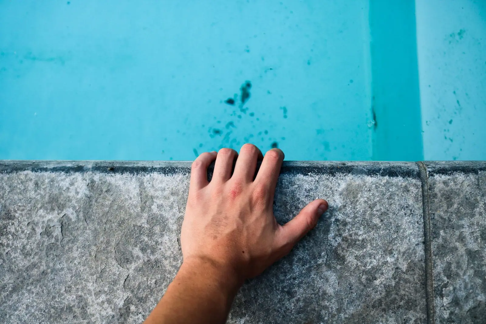 A hand resting on the tiled edge of a swimming pool