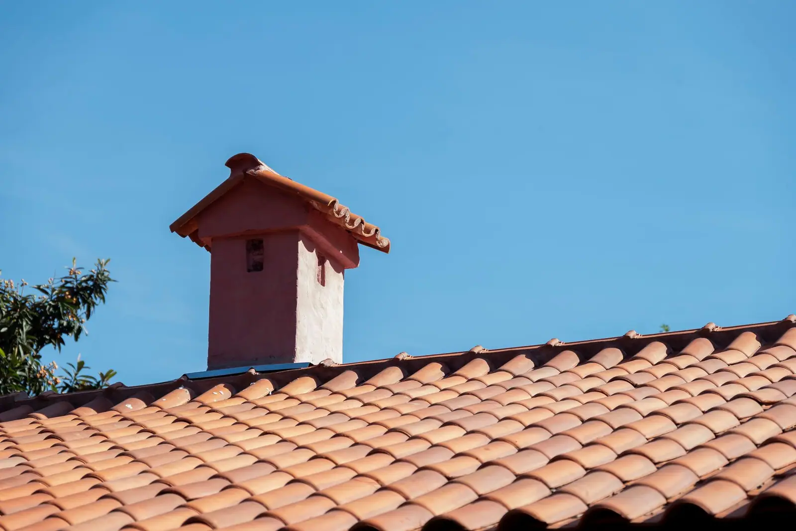 A pink chimney with a red tiled cap above a terracotta roof