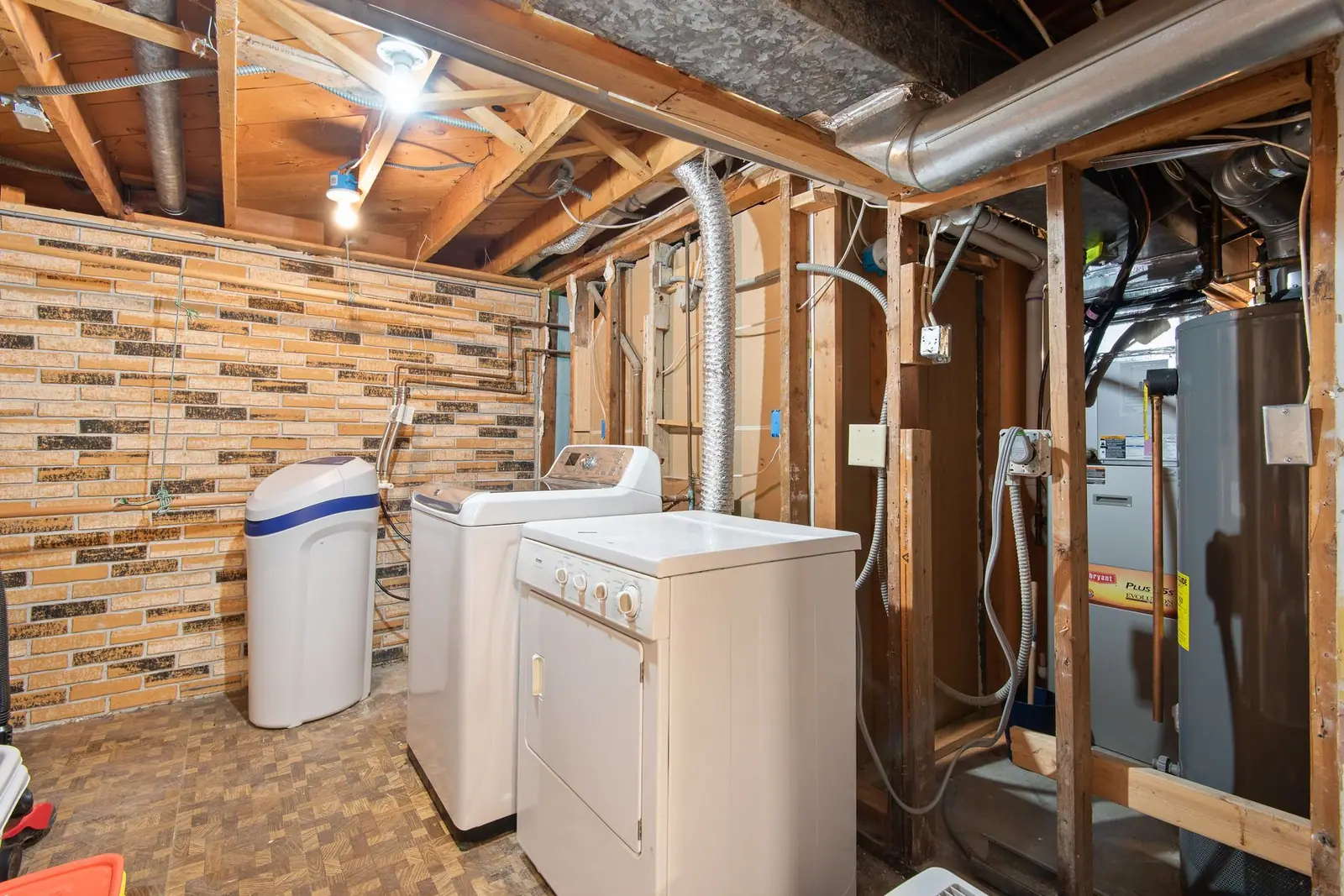 An unfinished basement with exposed joists, pipes and laundry machines