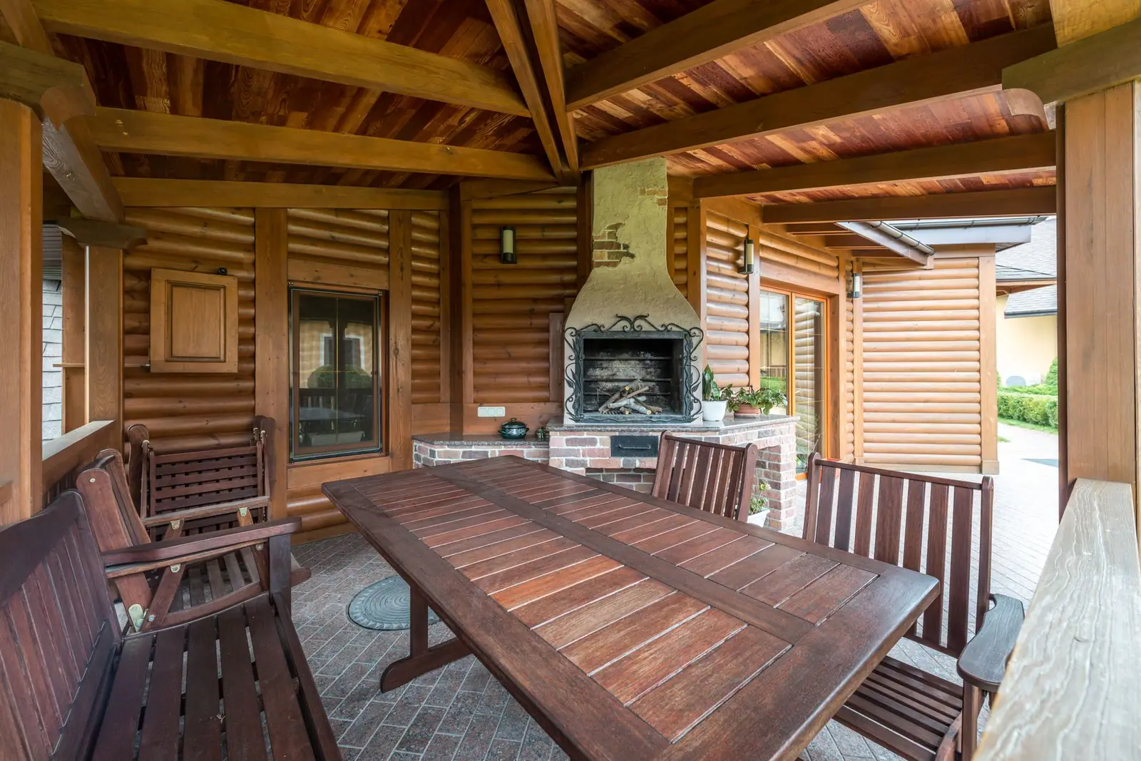 A covered wooden terrace with benches, a table and an outdoor fireplace