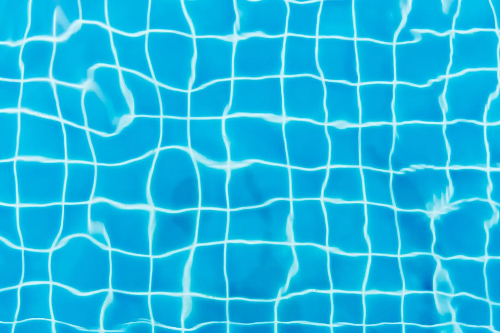 A tiled pool floor seen through clear blue water