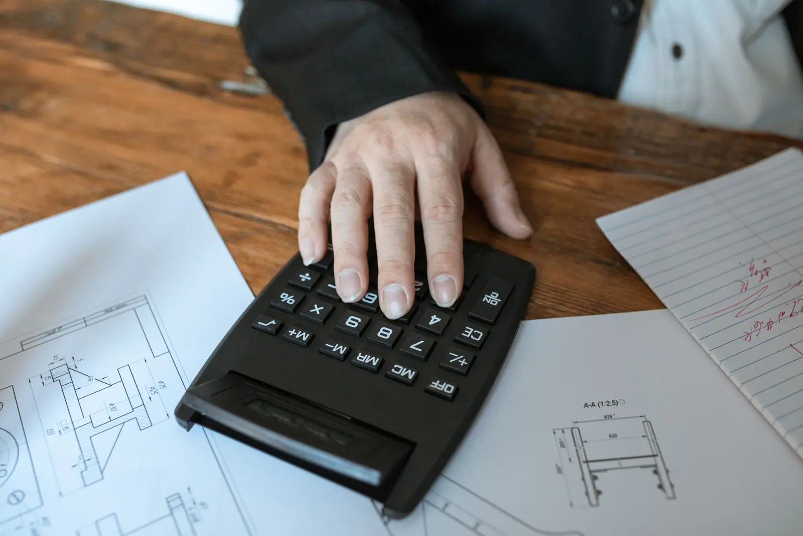 A hand using a calculator over a set of building plans
