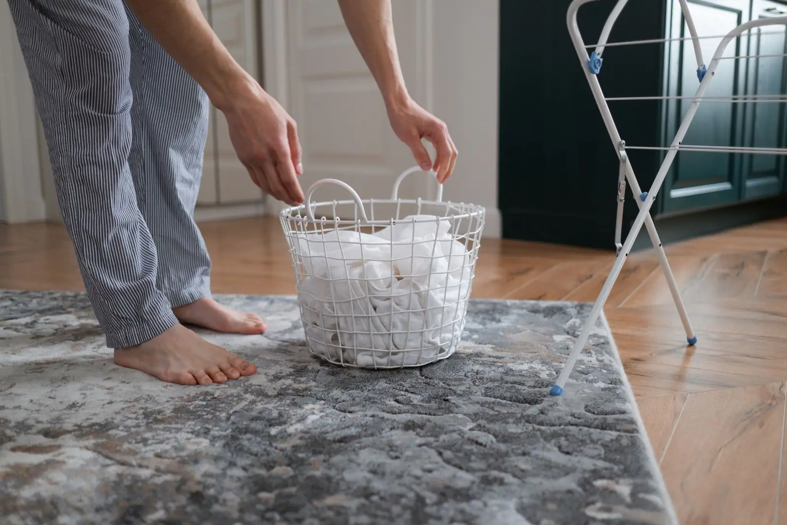 A person's bare feet beside a white laundry basket and indoor drying rack