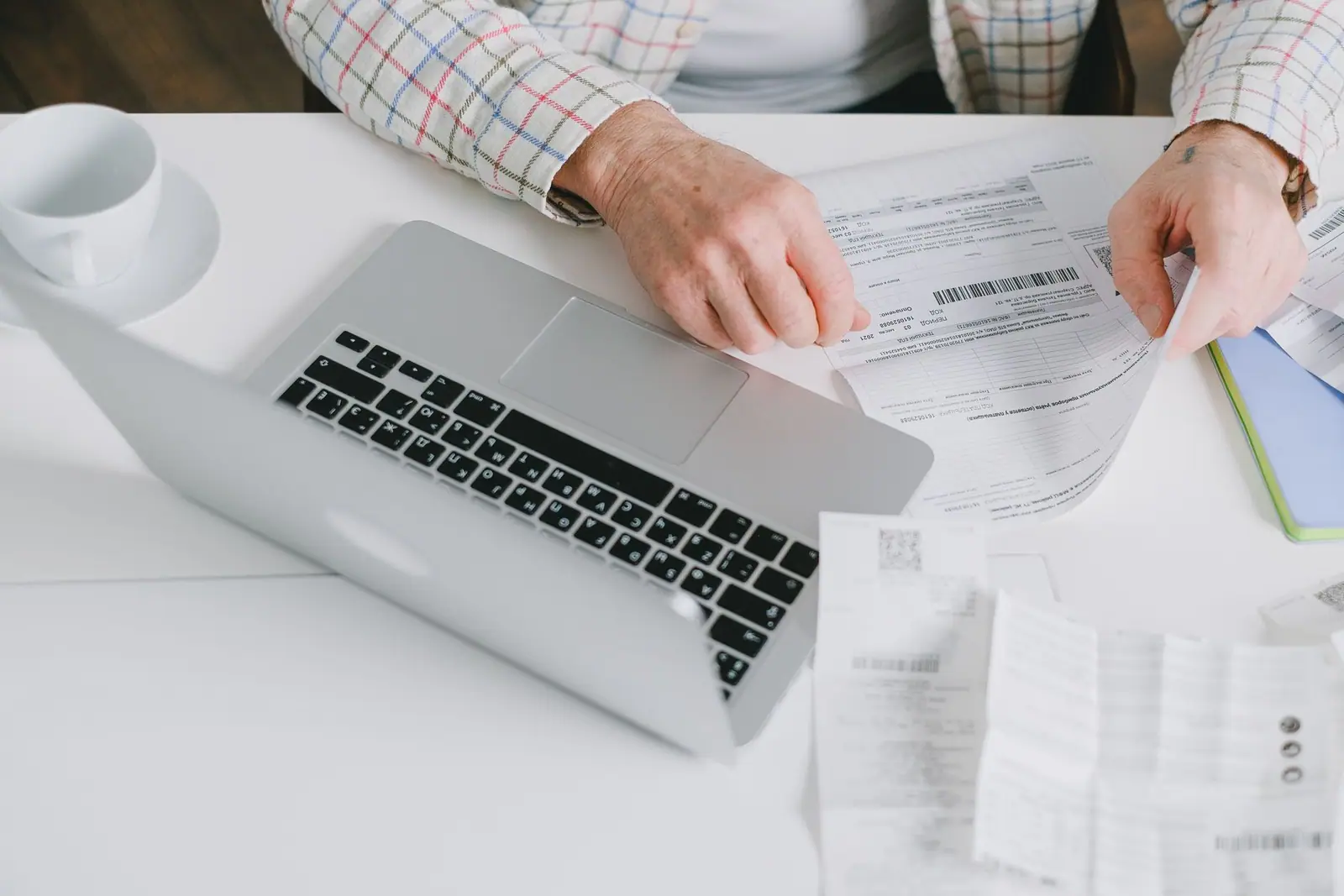 Hands reviewing a printed document beside a laptop on a white table
