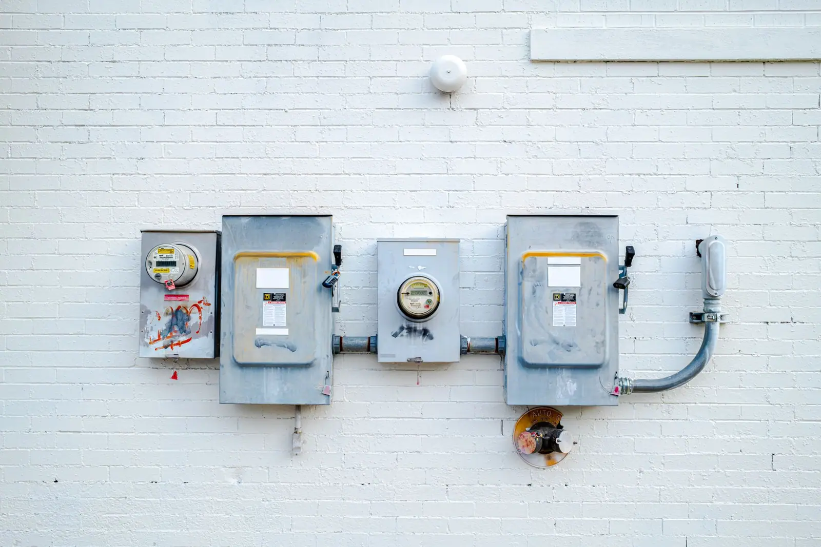 Utility electricity meters and their enclosures mounted on an exterior white brick wall