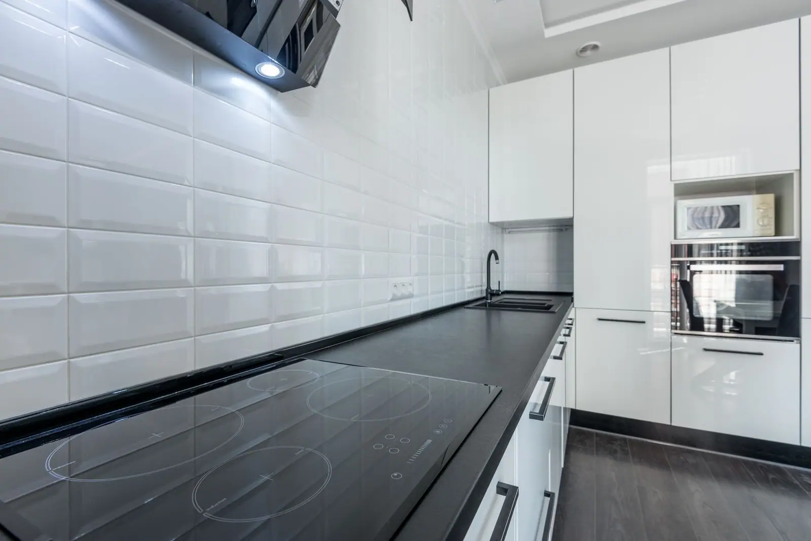 A kitchen with white cabinets, a black countertop, a range hood and a built-in wall oven