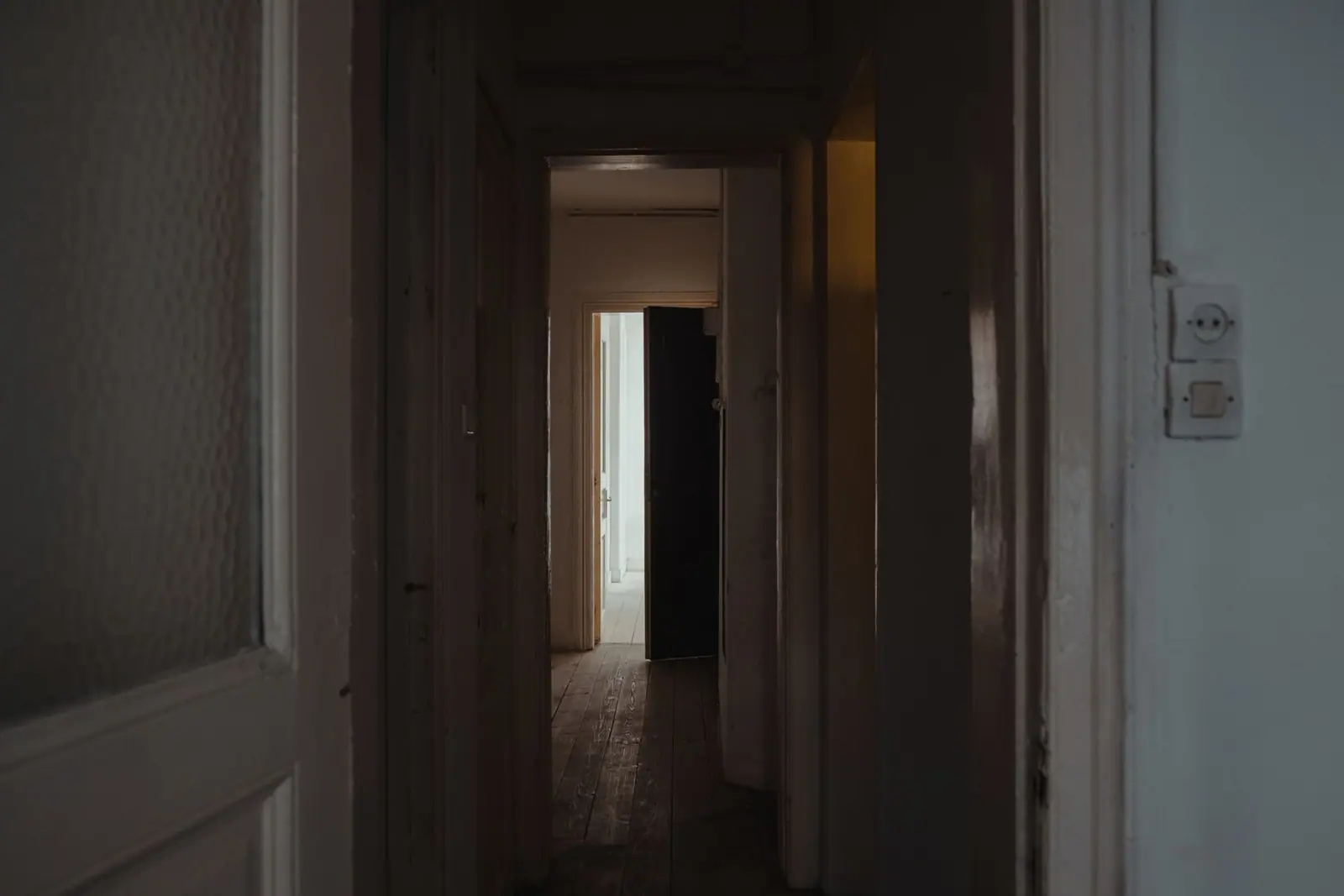 A dim hallway at night with light coming through a doorway