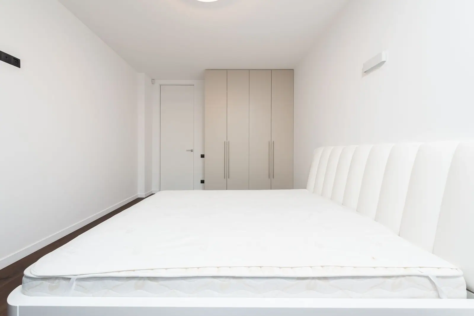 A white mattress seen from the foot of the bed in a minimalist bedroom
