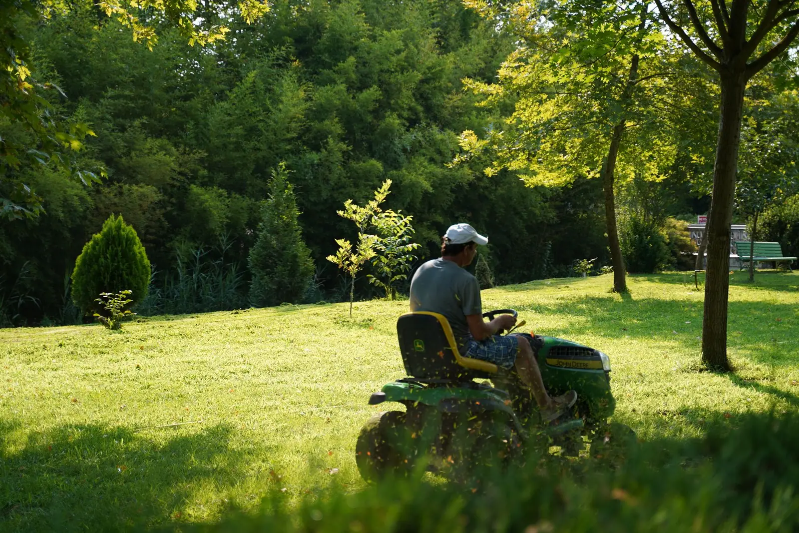 A person operating a green riding mower across a lawn