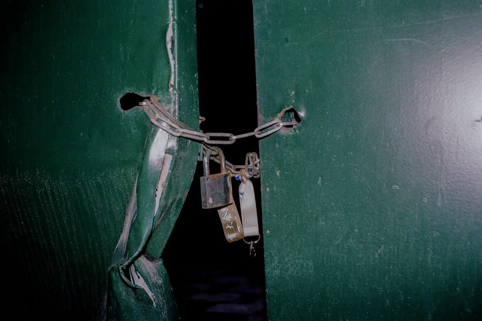 A padlock and chain securing a pair of green metal doors