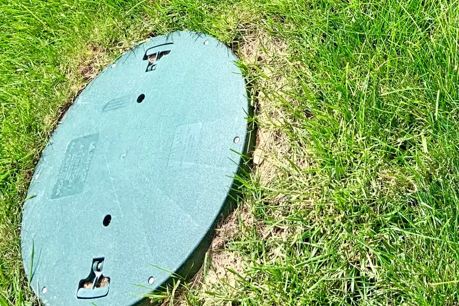 Three round green septic access covers beside a gray control box in grass