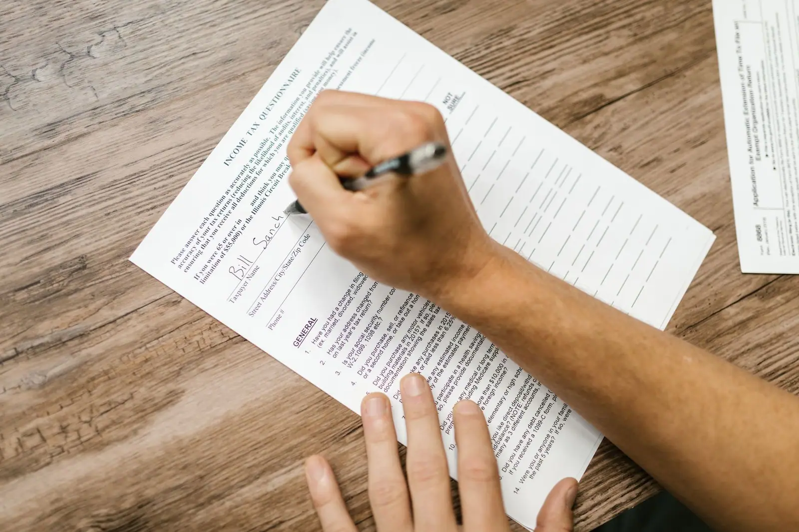 A hand filling in a printed form on a wooden table