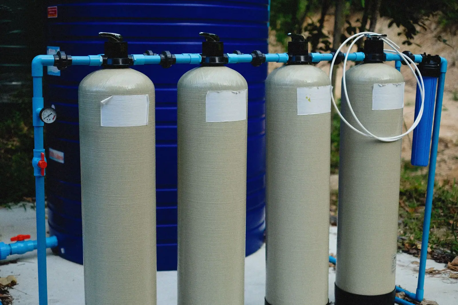Four beige water-treatment tanks with blue pipes outdoors