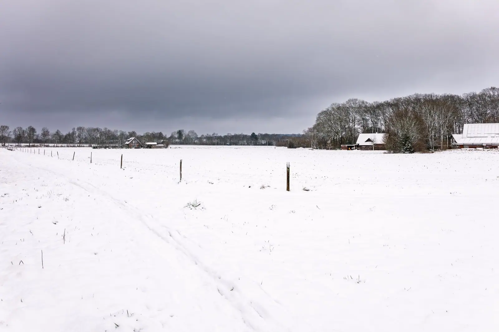 A snow-covered farm landscape under a cloudy sky